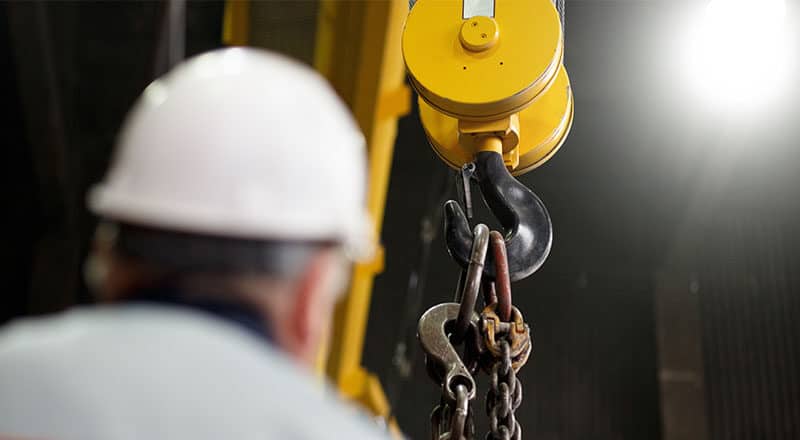 Worker in a white hard hat in front of an industrial hook.